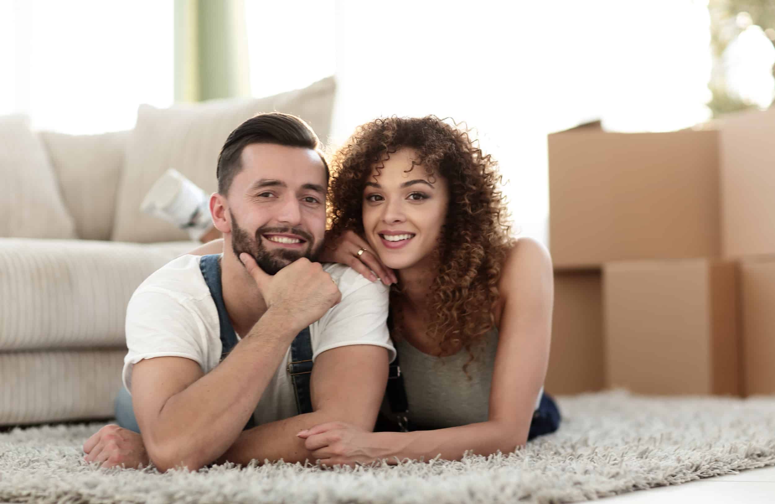 A young couple smiling in a new home surrounded by moving boxes