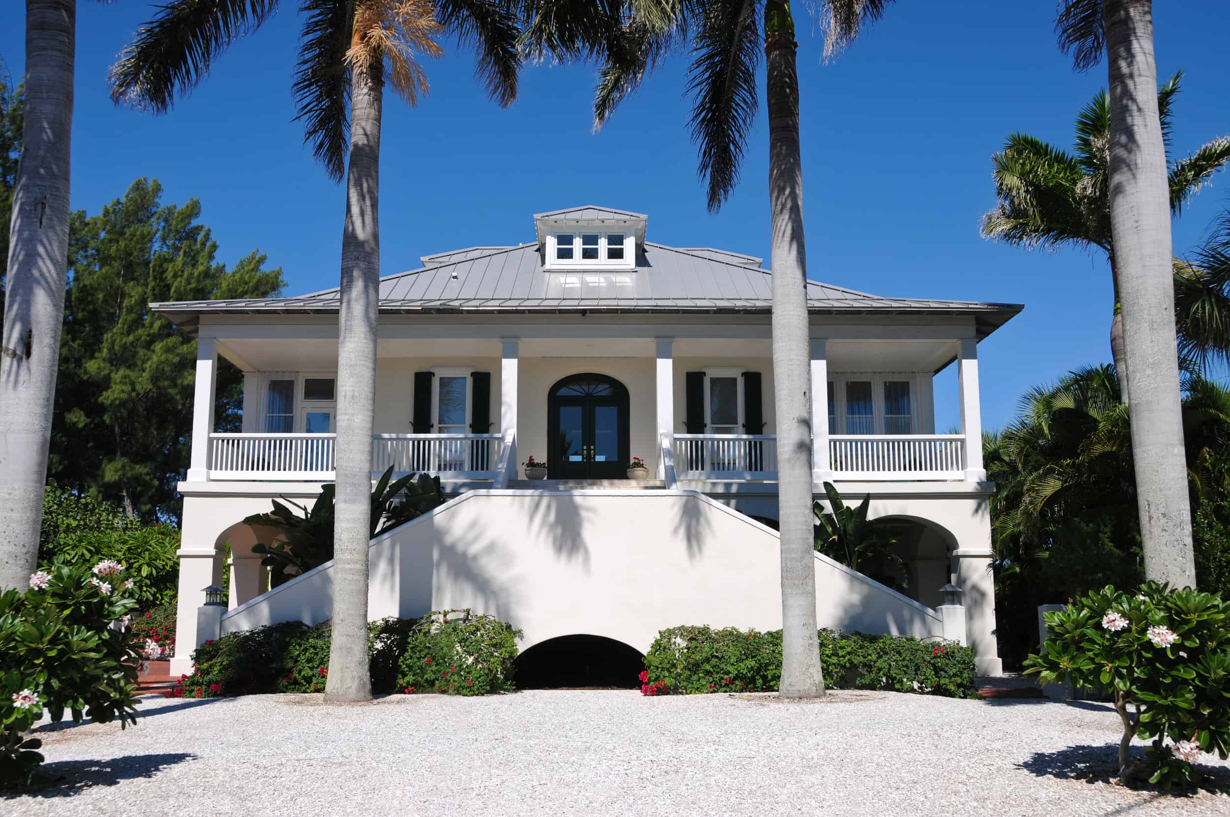 A large white Southern home with columns and palm trees